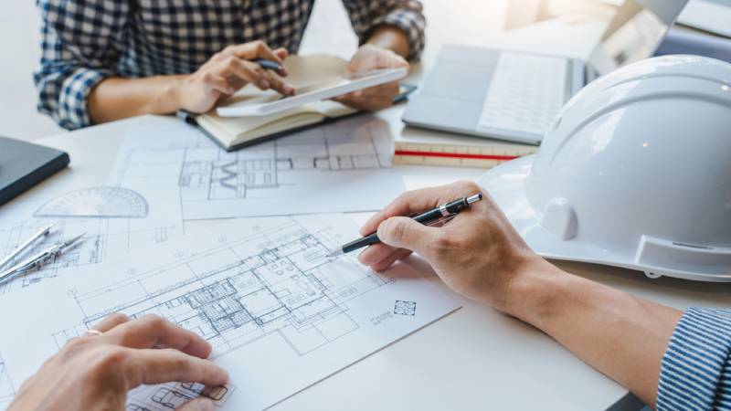 Close up of two architectural engineers work together on a drafting table.